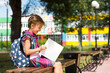 © Ольга Симонова - Girl with a backpack sitting on a bench and reading a book near the school. Back to school, lesson schedule, a diary with grades. Education, primary school classes, September 1