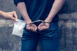 Drug dealer under arrest confined with handcuffs and hands at his back. Drug traffickers were arrested along with their heroin. Law and police concept.
