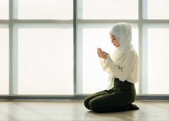 Wall Mural - Young and beautiful Asian Muslim woman sitting on floor and praying with respect and calm manner