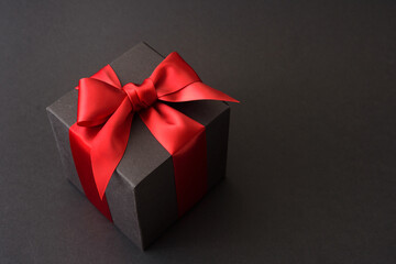 Black gift box with red bow on black background