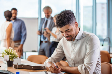 Portrait of confident young man at his desk with laptop doing paperwork. Happy african man at work. Cropped shot of a businessman working on a computer in an office