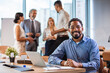 © Dragana Gordic - Portrait of happy successful executive with team working in background. Mature african businessman at meeting. Portrait of a professional businessman standing in an office with colleagues