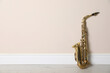 Beautiful saxophone on floor near beige wall indoors, space for text