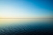 Tranquil minimalist landscape with a smooth blue sea surface with calm waters with a horizon and clear skies. Simple beautiful natural calm background. Copy space.