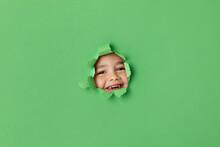 Smiling Boy Peeking Through Green Torn Paper