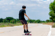 © Ekkasit A Siam - A back view of a young Asian man wearing a black shirt and pants is skateboarding on a rural road., Play surf skate.