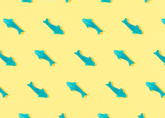 Summer pattern made with blue fish gummy candy on yellow background. Sunny day shadows. Flat lay.