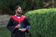 Portrait of handsome indian graduate student in graduation glow with diploma looking forward for copy space text