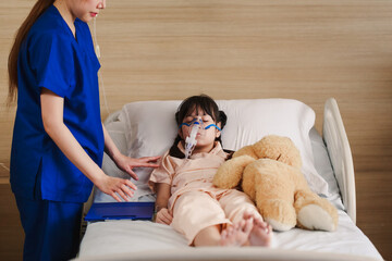 Young Asian female caregiver holding oxygen mask with cute girl patient in hospital. Nurse putting putting inhalation on the girl face.