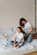 © Olena Serzhanova - Mother making braids to her daughter sitting on the bed at home.