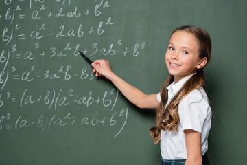 happy schoolkid pointing with pen at mathematic equations on chalkboard