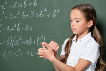 preteen schoolgirl counting on fingers near chalkboard with mathematic equations
