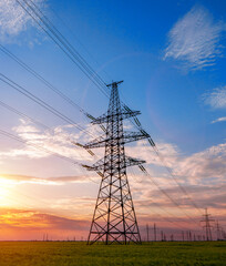 Wall Mural - high voltage lines and power pylons in a green agricultural field against a saturated sunset sky