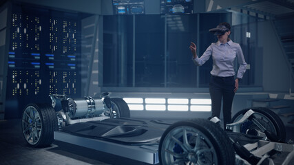 Mockup of Electric Vehicle: Automotive Female Professional Engineer working on design of Electric Car using Futuristic Augmented Reality Headset. High-tech facility. Electric car chassis.