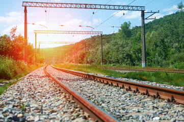 Morning landscape on the railway tracks. The sun's rays are the green grass and the rails on which the train travels. Trees along the railway.