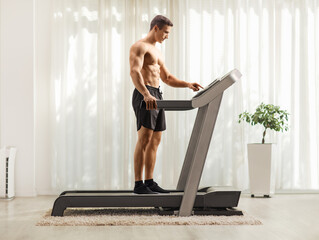 Wall Mural - Strong young man pushing a power switch on a treadmill in a room