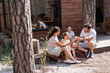 © Marharyta Hanhalo - Mom and dad clink glasses of juice or cool lemonade during a summer picnic, sitting on the porch of a wooden house with two children, a girl and a boy.