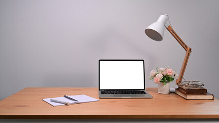 Laptop computer with blank screen, notebook and lamp on wooden table.