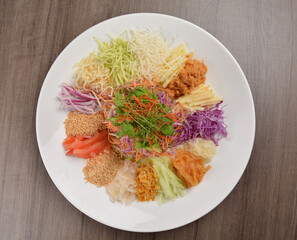 Wall Mural - Chinese New Year festival colourful Yu Sheng Lo Hei salad with smoked salmon fish, cracker cookies and sweet sauce on wood background asian halal menu