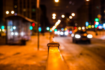 Wall Mural - Winter night in the big city, the bus stop and the stream of cars. Close up view from the handrail on the sidewalk level