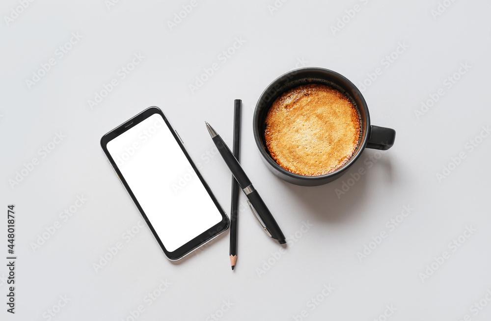 Cup of coffee with mobile phone and stationery on light background