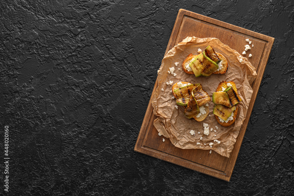 Tasty bruschettas with cheese and grilled zucchini on dark background