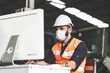 © NVB Stocker - Young caucasian engineering man worker working on digital tablet computer at manufacturing. Worker man wearing face mask prevent covid-19 virus and protective hard hat.