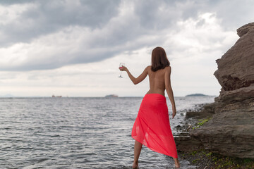 Wall Mural - Woman in a red dress with glass of red wine on a beach.