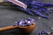 Dripping of lavender essential oil into spoon with flowers on dark background