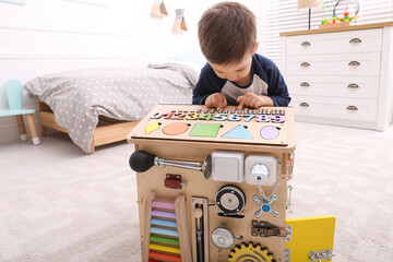 Wall Mural - Little boy playing with busy board house on floor at home