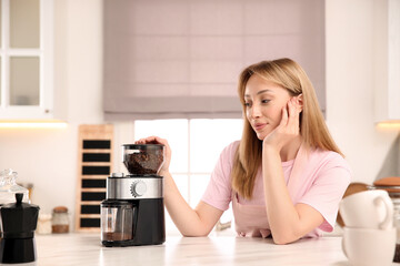 Poster - Young woman using electric coffee grinder in kitchen