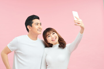 Wall Mural - Happy young couple makes selfie, dressed in stylish clothes on pink background