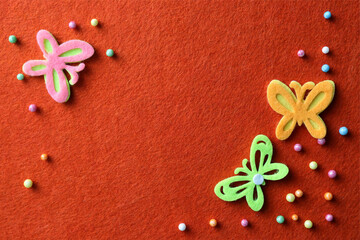 Sticker - Small colorful beads and felt butterflies on red background, flat lay. Space for text