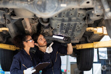 Hispanic Female Trainee Mechanics Working Underneath Car Together Car Maintenance And Auto Service Garage. Car Maintenance And Auto Service Garage Concept.