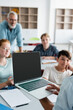 © LIGHTFIELD STUDIOS - Schoolboy holding laptop near blurred multiethnic classmates and teacher