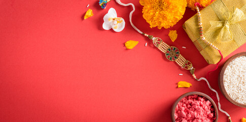 Raksha Bandhan, Indian festival with beautiful Rakhi and  Rice Grains on red background.  A traditional Indian wrist band which is a symbol of love between Sisters and Brothers.