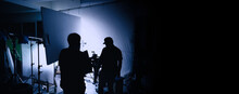 Video Production Behind The Scenes. Making Of TV Commercial Movie That Film Crew Team Lightman And Cameraman Working Together With Film Director In Studio. Film Production Concept. Silhouette Style.