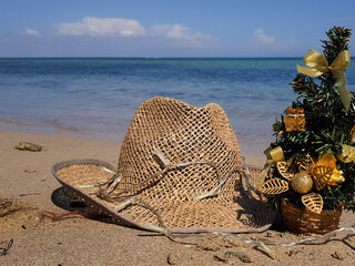 in summer, a straw hat lies on the sand on the beach. Christmas tree next to the background of the sea. the New Year holidays