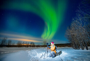 photographer man with camera and tripod photographs aurora borealis, northern lights green. concept 