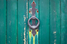 Detail Of Old Wooden Door With Vertical Stripes And Rustic Iron Ring Pull Handle Or Knocker With Fleur-de-lis Design . Background Painted In Tones Of Green Or Teal Color With Empty Space For Text