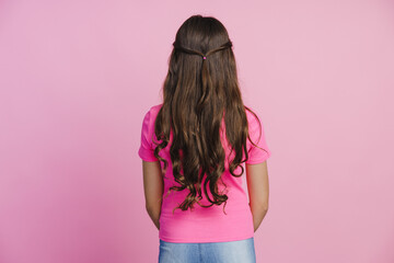 back view of a girl with long hair, beautiful hairstyle on a pink wall background. cute little girl 