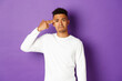 Image of sad and tired african-american male student, making finger gun sign over head and shooting himself, standing distressed against purple background