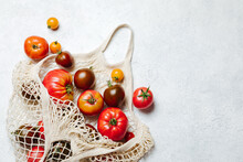 Fresh Colorful Heirloom Veriety Tomatoes In Eco Friendly Mesh Shopping Bag On White Concrete Background. Zero Waste