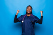 © F8  \ Suport Ukraine - Waist up portrait of strong successful determined young African American doctor woman raising arms, clenching fists, exclaiming with joy and excitement.