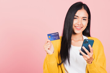 Wall Mural - Happy Asian portrait beautiful cute young woman excited smiling hold mobile phone and plastic debit credit bank card, studio shot isolated on pink background, female using smartphone online shopping