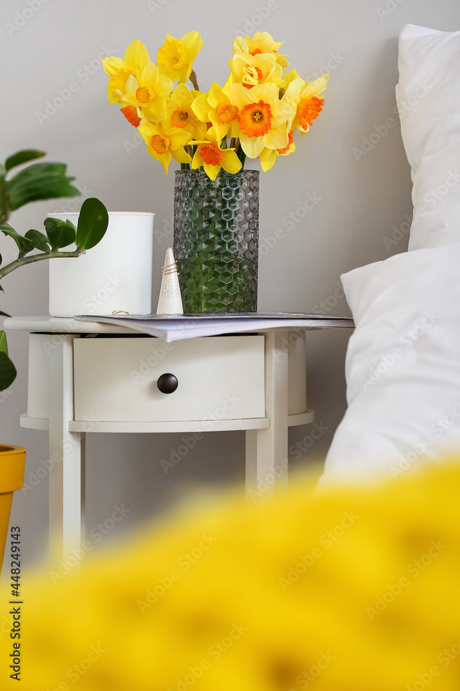 Vase with narcissus flowers on bedside table in room