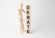 Wooden mannequin near tower of cubes with word debate on table against light background