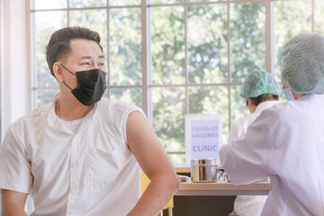 Wall Mural - Portrait of man looking at while getting covid vaccine in clinic or hospital, with hand nurse injecting vaccine to get immunity for protect virus. teenager wearing protective mask.