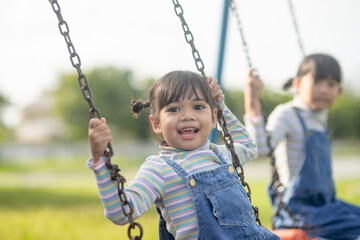 Happy little Asian girl playing swing outdoor in the park