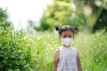 Wall Mural - Cute small girl with protective face mask standing at field.